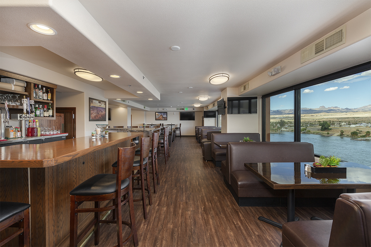 A wide view of a bar with a long counter, booths, and a view of a river.