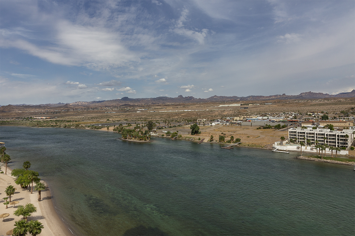 A wide aerial view of a lake or river with a sandy beach and buildings in the background.